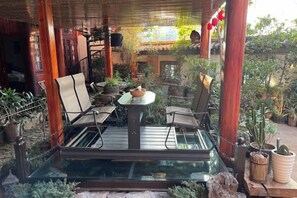 En uteplats med ett glasbord omgivet av stolar, krukväxter och träpelare.