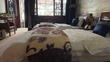 A hotel room with three beds, a wooden desk, and a large window with a view of the outside.