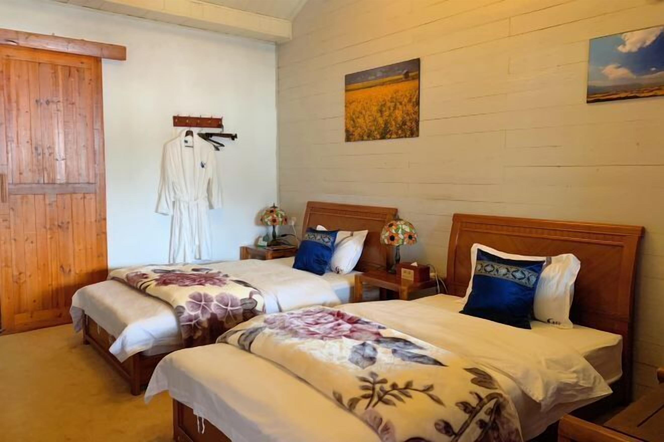 A room with two beds, wooden headboards, a wooden door, and a wall-mounted coat rack.