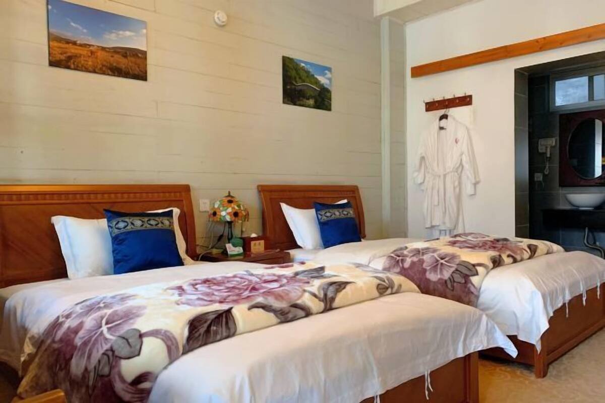A hotel room with two beds, a wooden headboard, a nightstand with a lamp, and a view of the outdoors.
