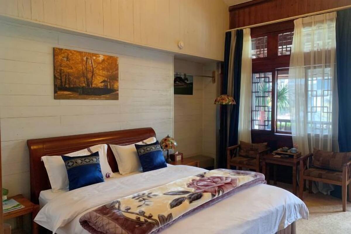 A bedroom with a wooden headboard, a bed with floral bedding, a nightstand, a chair, and a window with curtains.