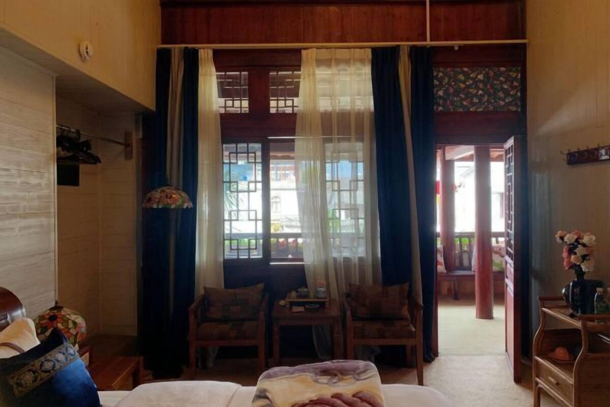 A room with a bed, a table, chairs, and a view through a window with curtains.
