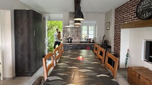Moderni keittiö, jossa on tummat kaapit, ruokailutila kuviollisella pöytäliinalla sekä tiiliseinä, jossa on kello.