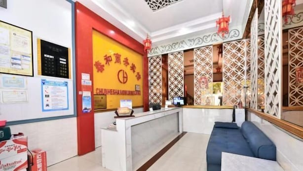 Un hall d’accueil d’hôtel avec un mur rouge et jaune, un comptoir d’accueil, un canapé bleu et des paravents décoratifs.