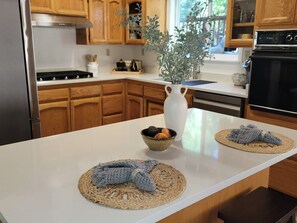 Una cocina con armarios de madera, encimera blanca, refrigerador de acero inoxidable y horno negro.