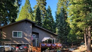A two-story cabin with a porch decorated with a flag, surrounded by trees. - Lake Almanor West home in a peaceful setting just minutes from the lake (Chester)