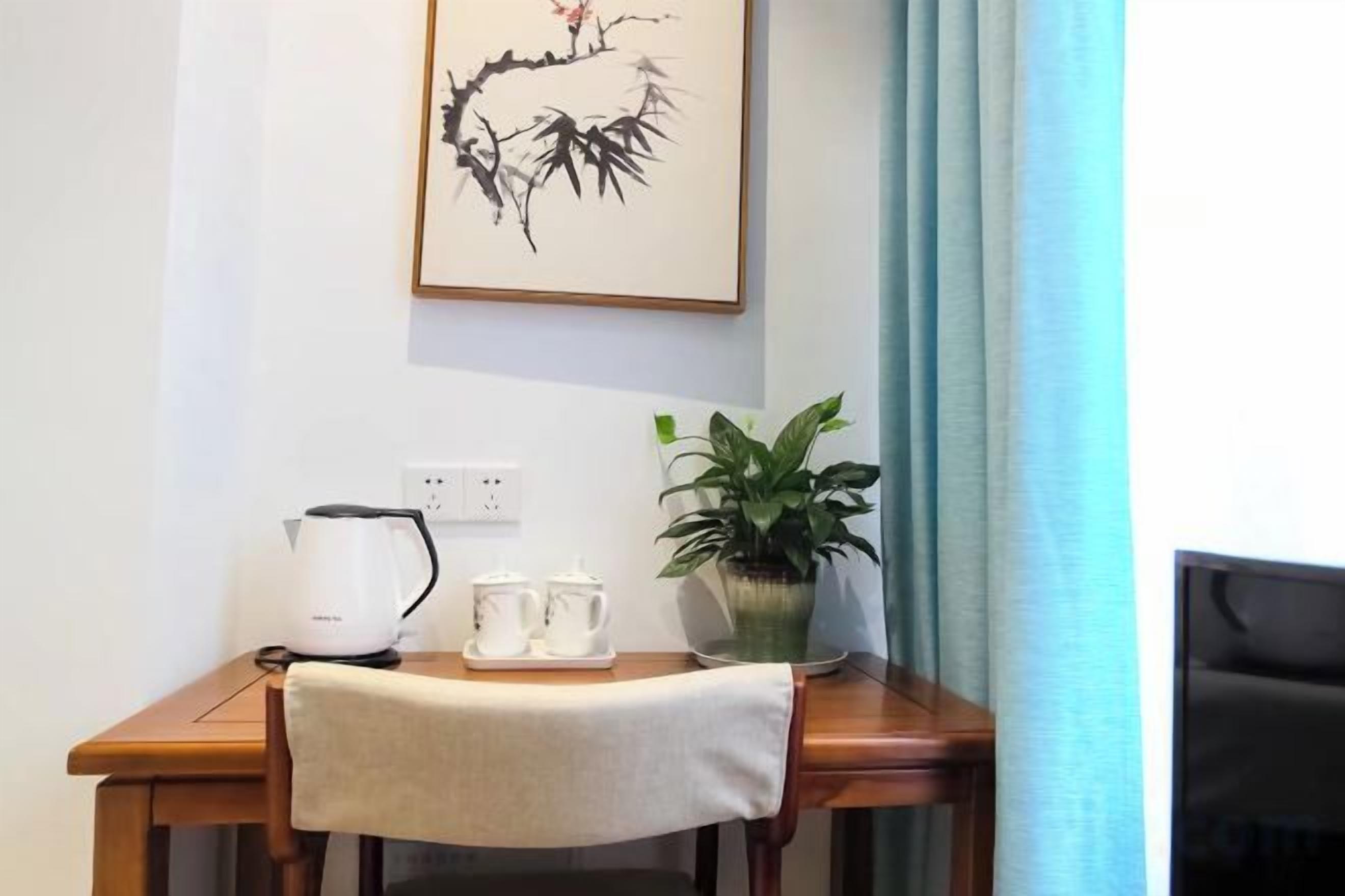 A wooden table with a kettle, teapot, and cups, a potted plant, and a framed artwork on the wall.
