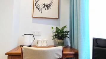 A wooden table with a kettle, teapot, and cups, a potted plant, and a framed artwork on the wall.