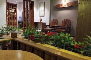 A room with a wooden table, chairs, a bookshelf, and potted plants. - Banmu Yuntian Inn (Fenghuang County)