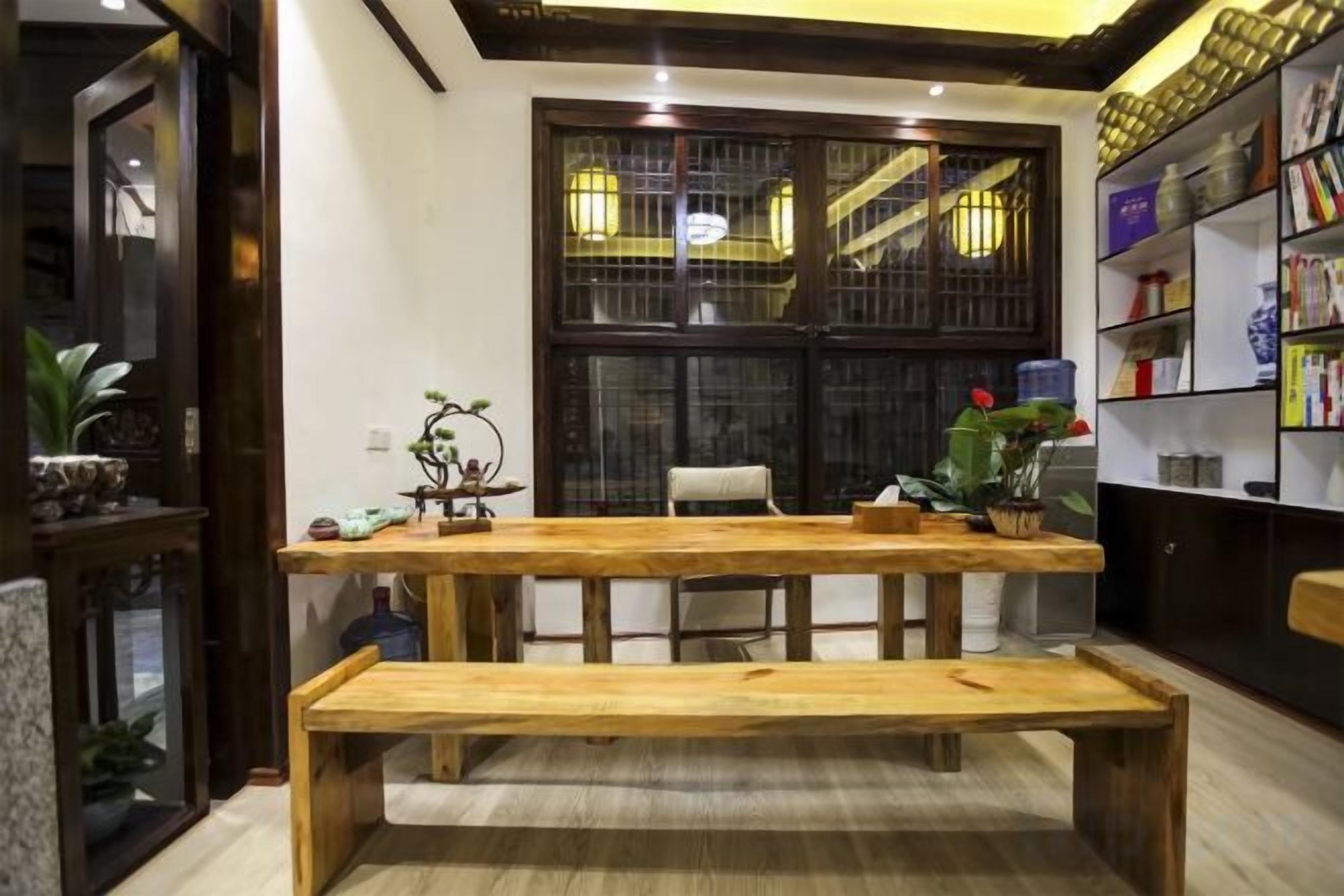 Una habitación con una mesa de madera, sillas, un banco, una estantería y un ventanal con detalles decorativos.