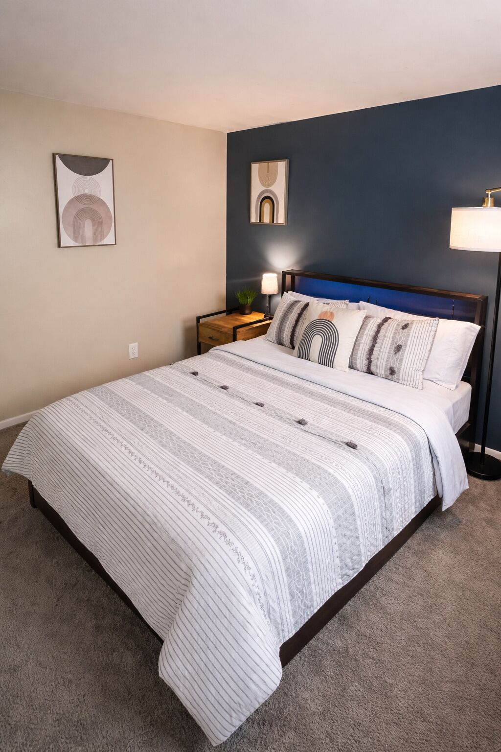 A bedroom with a bed, nightstands, a lamp, and wall art.