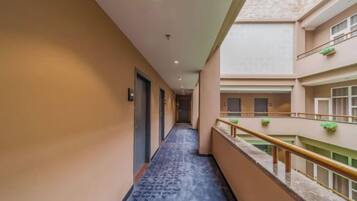 A hotel corridor with a blue patterned carpet, a balcony with a railing, and a view of the building's interior.