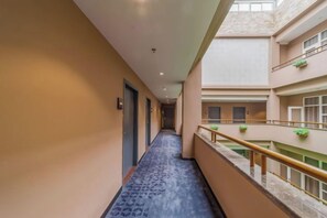 Een hotelgang met een blauw tapijt met patroon, een balkon met een leuning en uitzicht op het interieur van het gebouw.