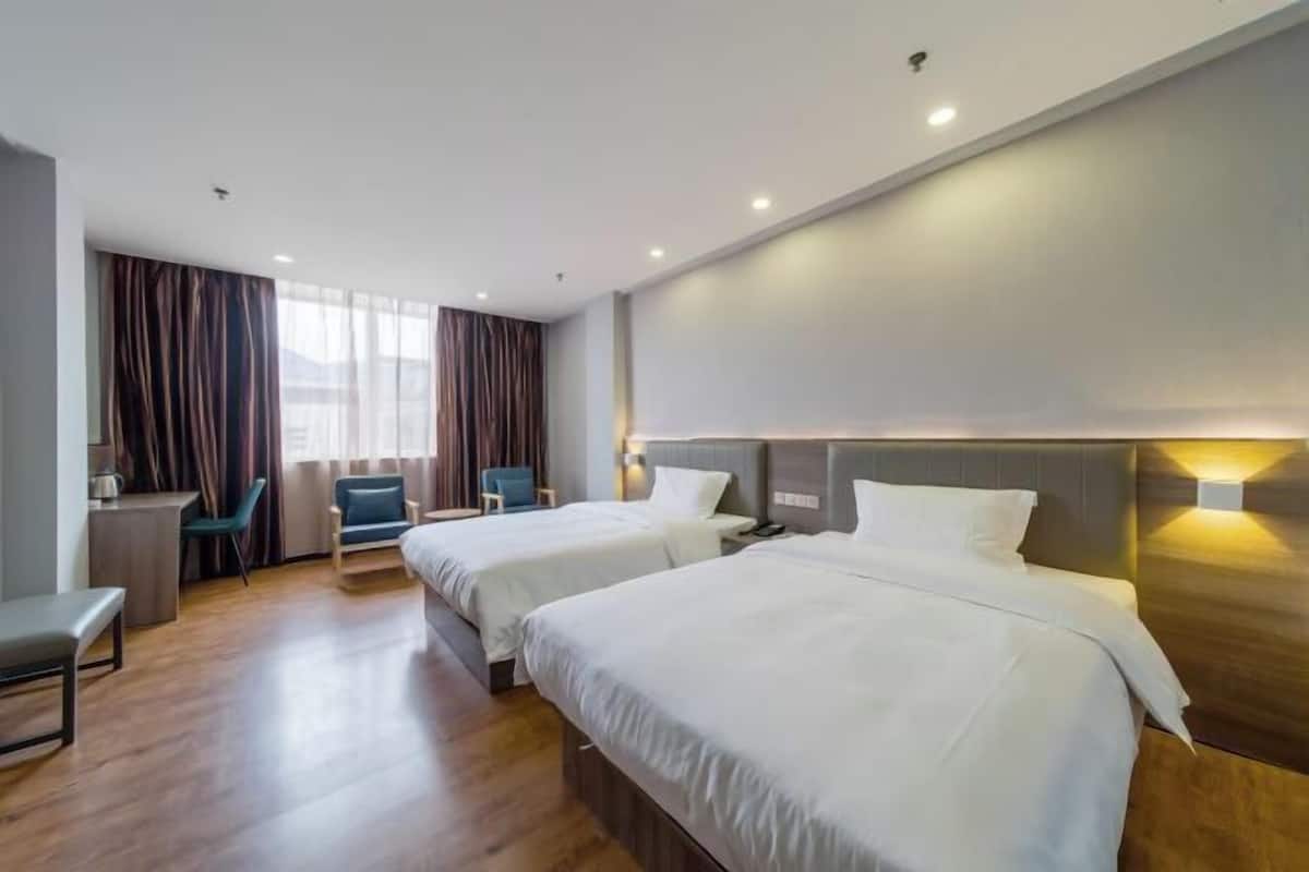 Quarto de hotel com duas camas, uma escrivaninha, cadeiras e uma janela grande com cortinas.