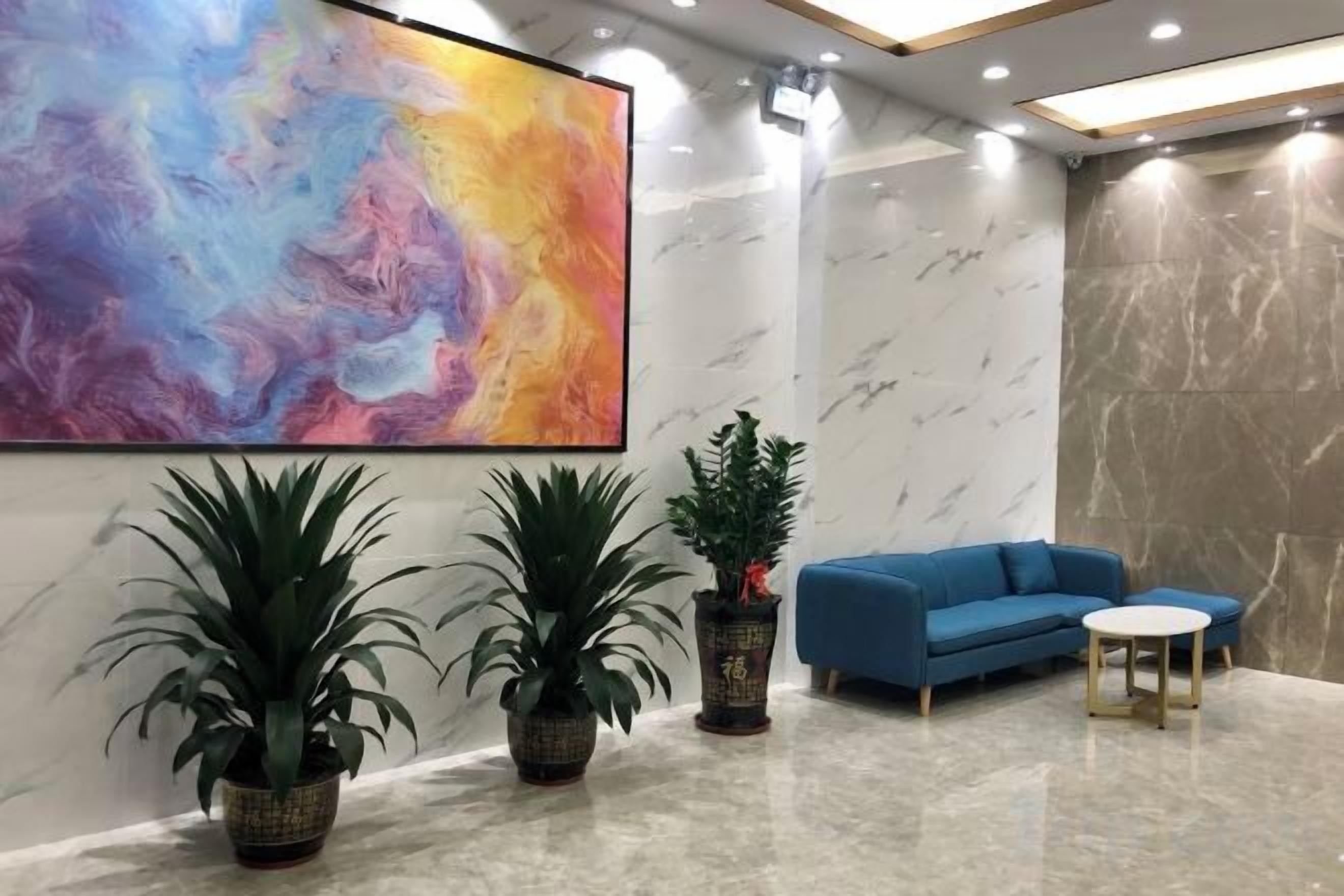 A modern lobby with a large abstract painting, a blue sofa, a small round table, and two potted plants.