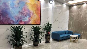 A modern lobby with a large abstract painting, a blue sofa, a small round table, and two potted plants.