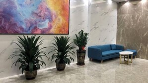 Un hall d’entrée moderne agrémenté d’un grand tableau abstrait, de deux plantes en pot, d’un canapé bleu et d’une petite table ronde.