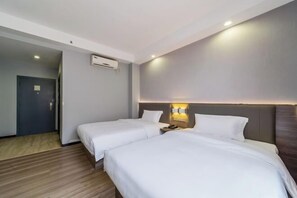 Ein Hotelzimmer mit zwei Betten, einem Nachttisch mit Lampe, einer Klimaanlage und einer Tür.