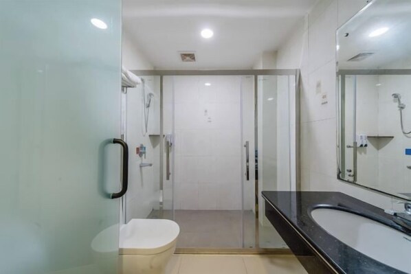 Ein modernes Badezimmer mit Duschkabine aus Glas, einer weißen Toilette und einem schwarzen Waschbecken mit großem Spiegel.