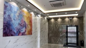 Un hall d’entrée moderne avec un sol en marbre, une peinture abstraite aux couleurs vives et un ascenseur.