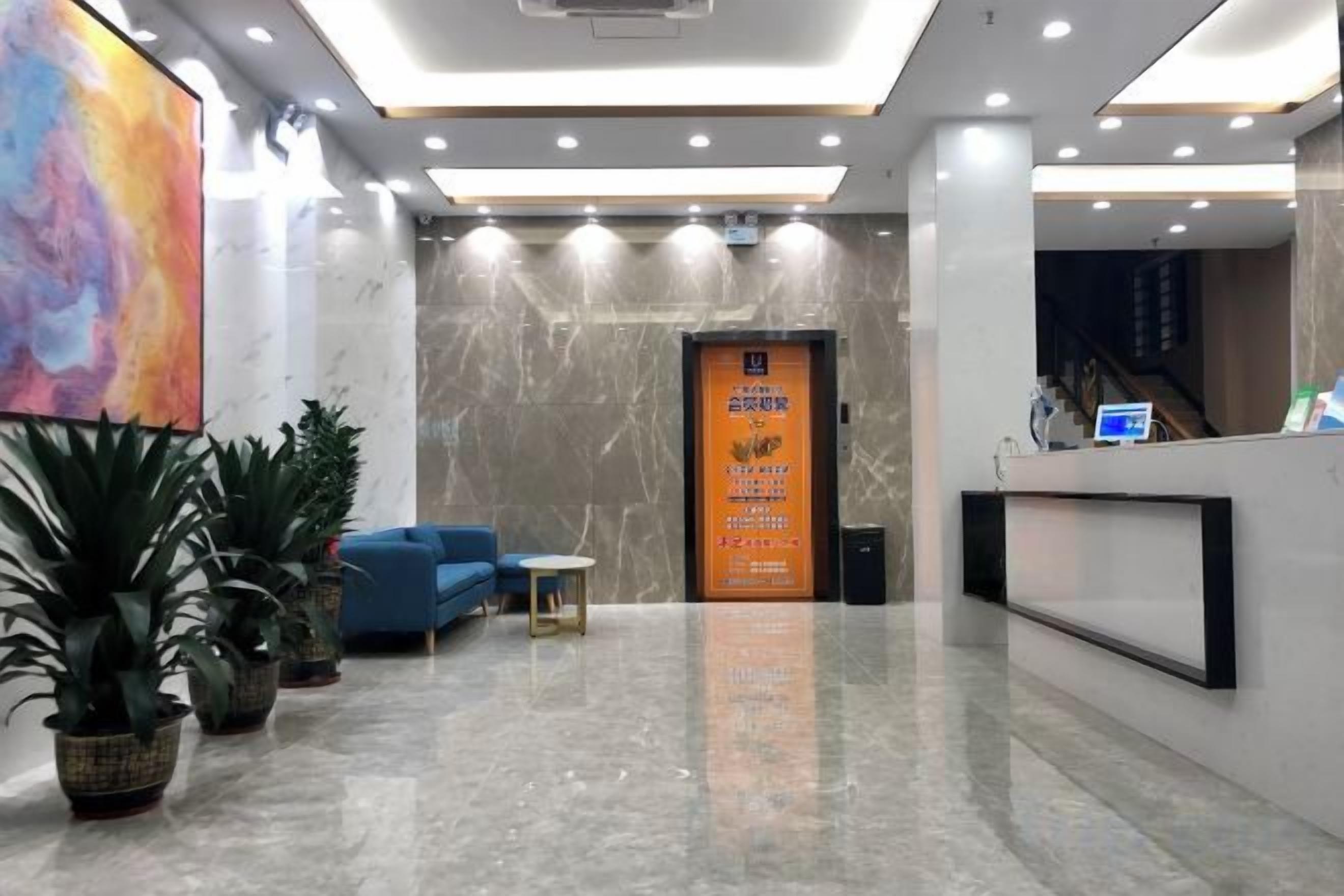 A hotel lobby with a reception desk, seating area, and a large painting on the wall.