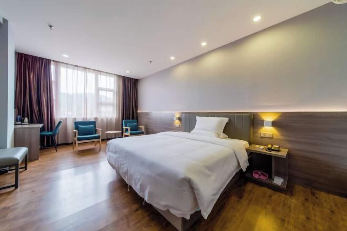 Quarto de hotel moderno com uma cama grande, uma escrivaninha, duas cadeiras e uma mesa de cabeceira com abajur.
