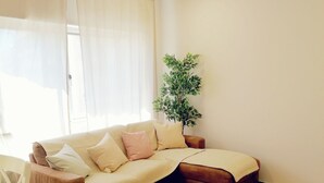Un salon avec un canapé d’angle marron, un tapis rond en fibres naturelles, une table basse en bois et une plante en pot.