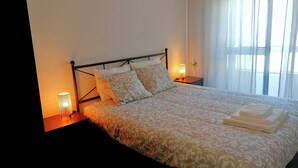 Un lit bien fait, avec une couvre-lit à motifs et des oreillers, une lampe de chevet et un vase avec une fleur posé sur une table de chevet.