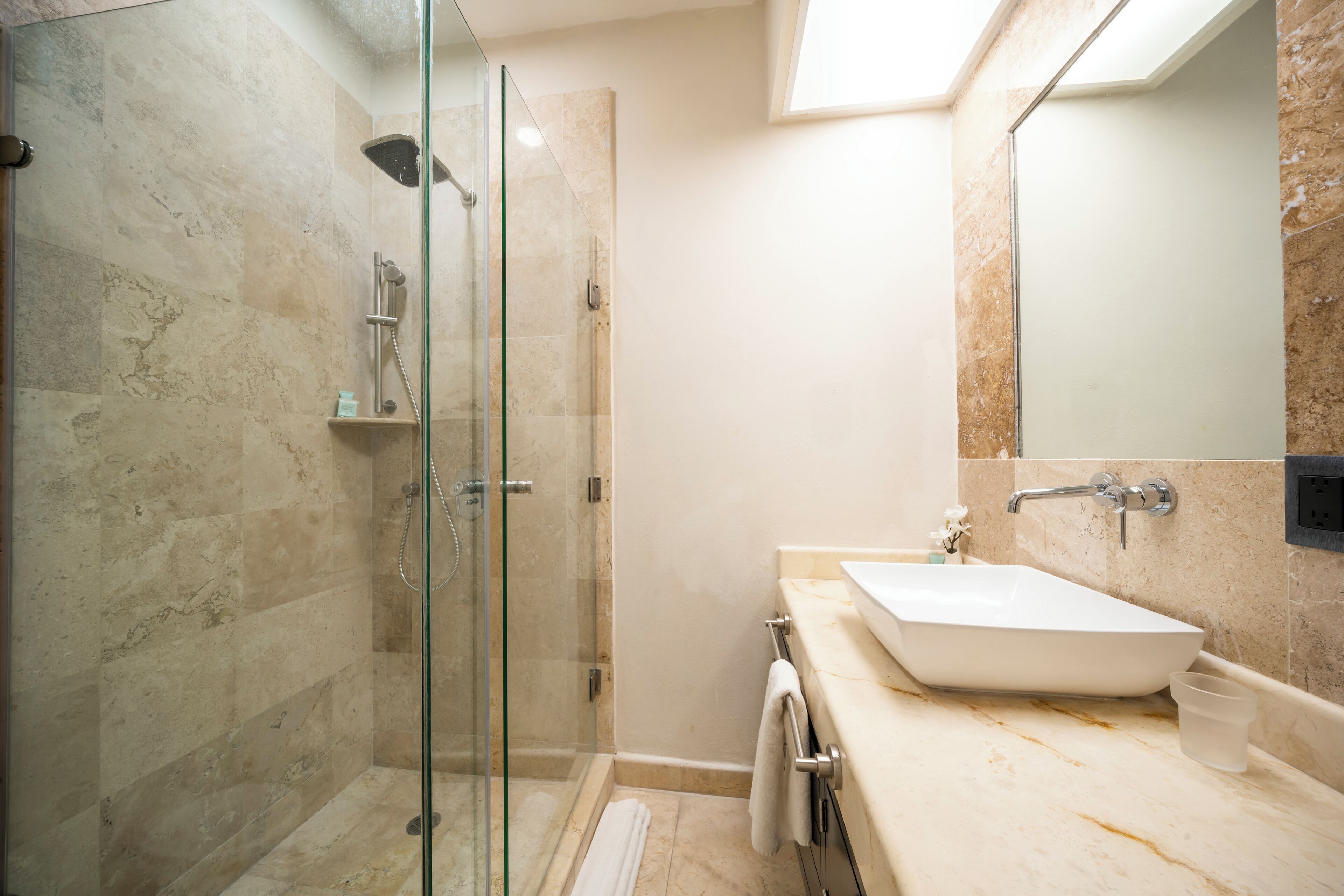 Un baño moderno con ducha envuelta en vidrio, un lavabo blanco y un espejo grande.