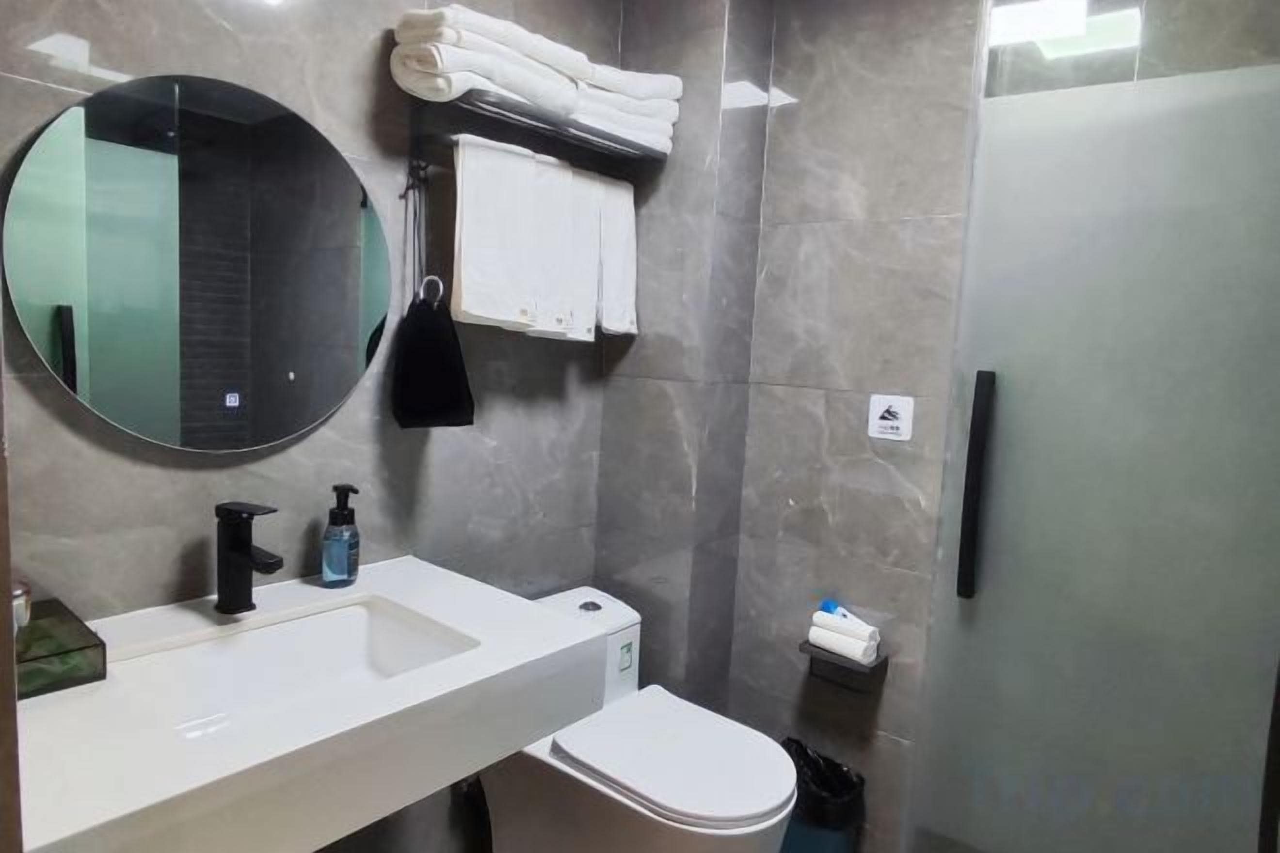 Ein Badezimmer mit einem weißen Waschbecken, einem runden Spiegel, einer Toilette und einer Duschkabine aus Glas.