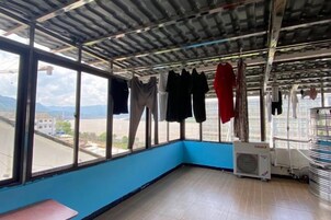 Una habitación con un ventanal grande, pared azul y techo de metal. Ropa colgada en un tendedero.