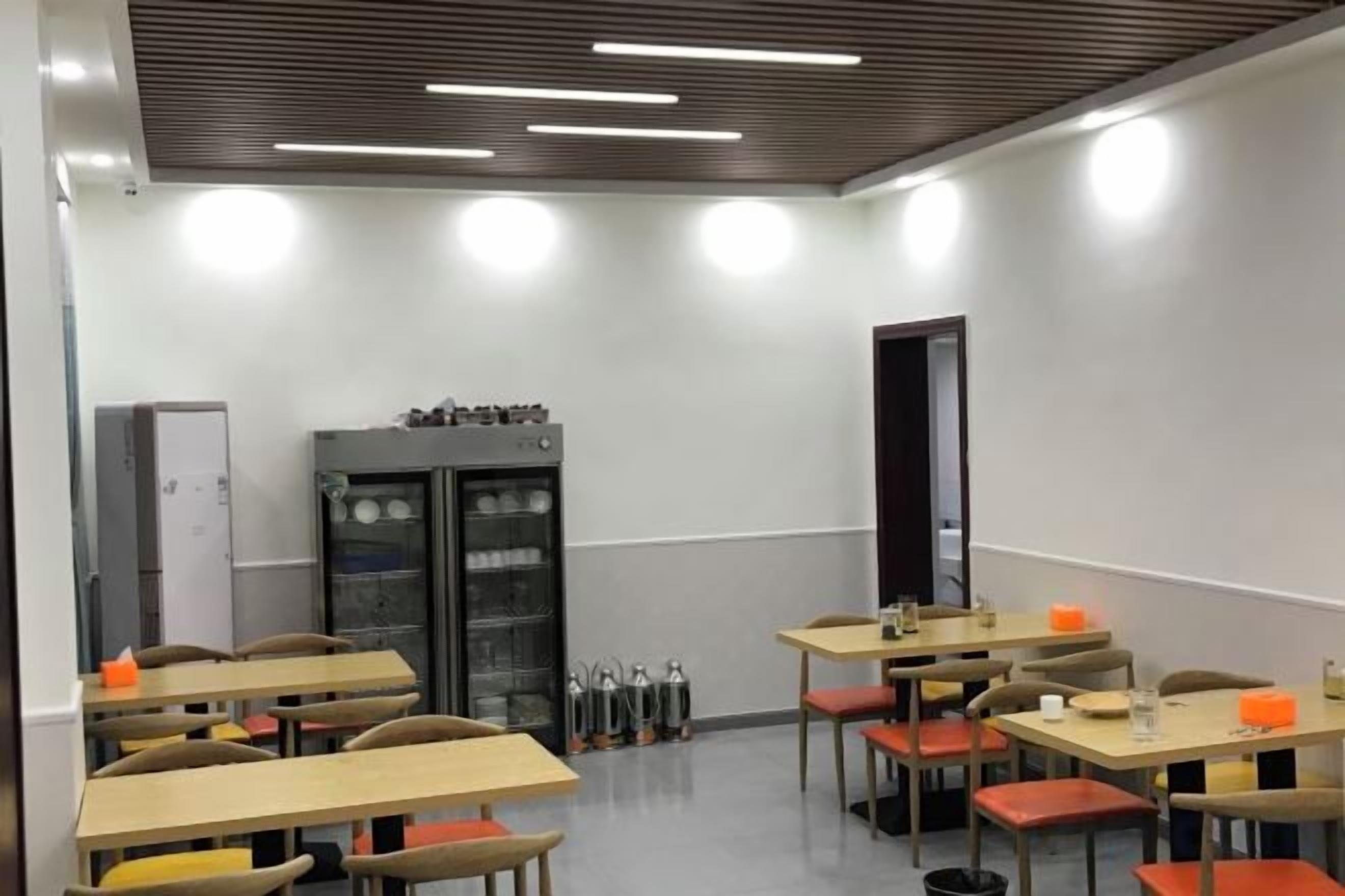 Un aula con mesas, sillas, un refrigerador y una puerta.