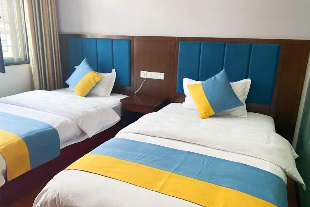 Deux lits jumeaux avec une literie bleue et jaune, une tête de lit en bois et une table de chevet placée entre les deux.