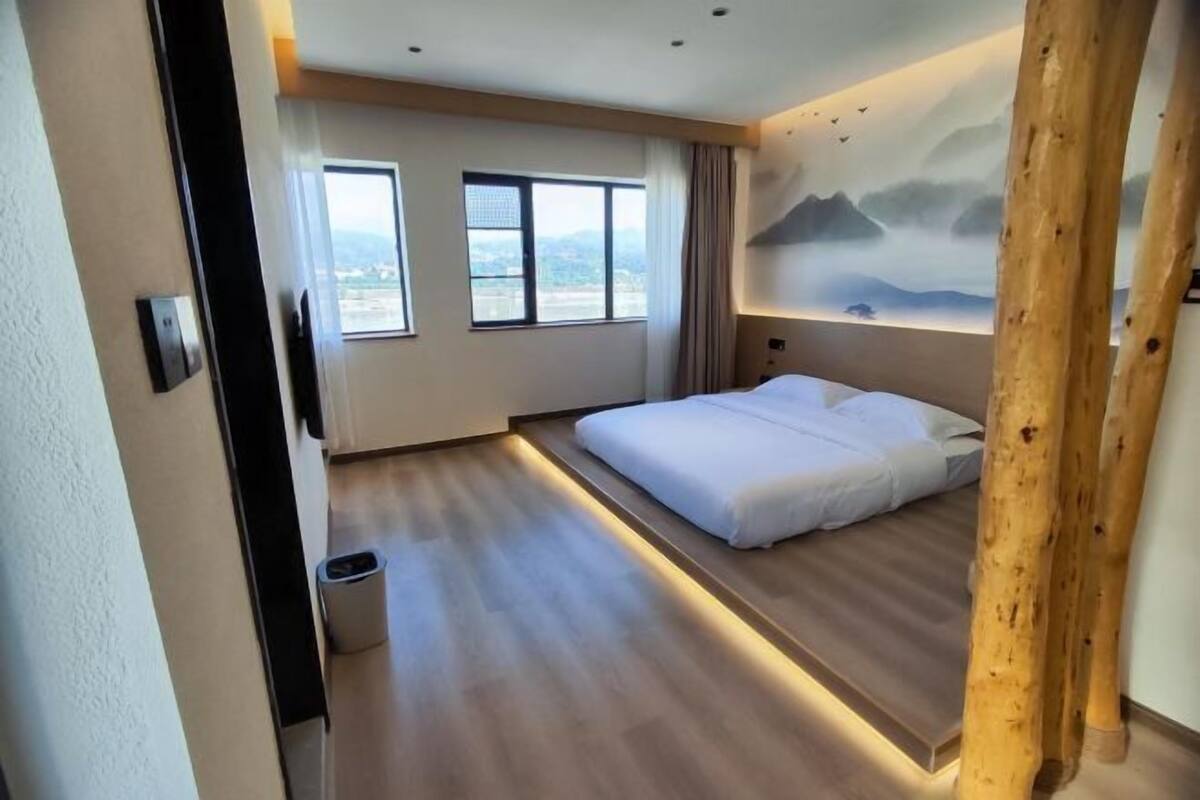 Une chambre d’hôtel moderne avec un grand lit, deux fenêtres et une vue sur le paysage urbain.