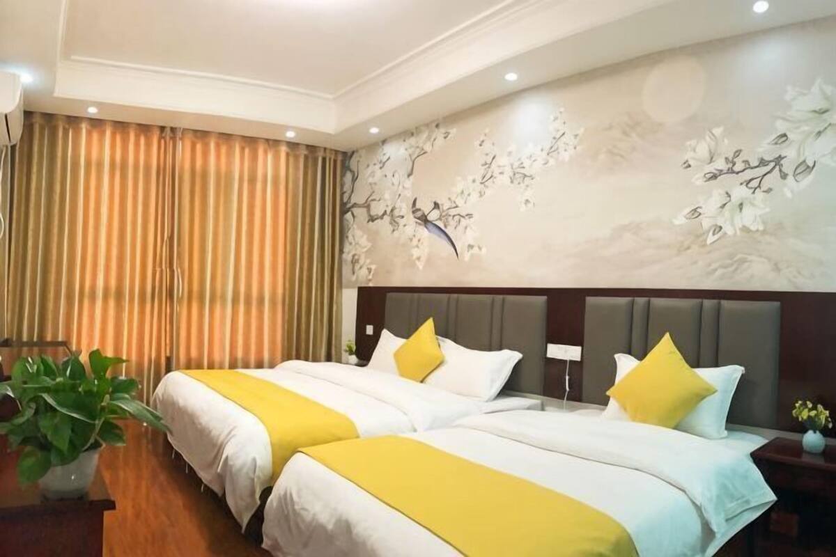 Une chambre d’hôtel avec deux lits, une table de chevet, une plante en pot et une fresque décorative sur le mur.