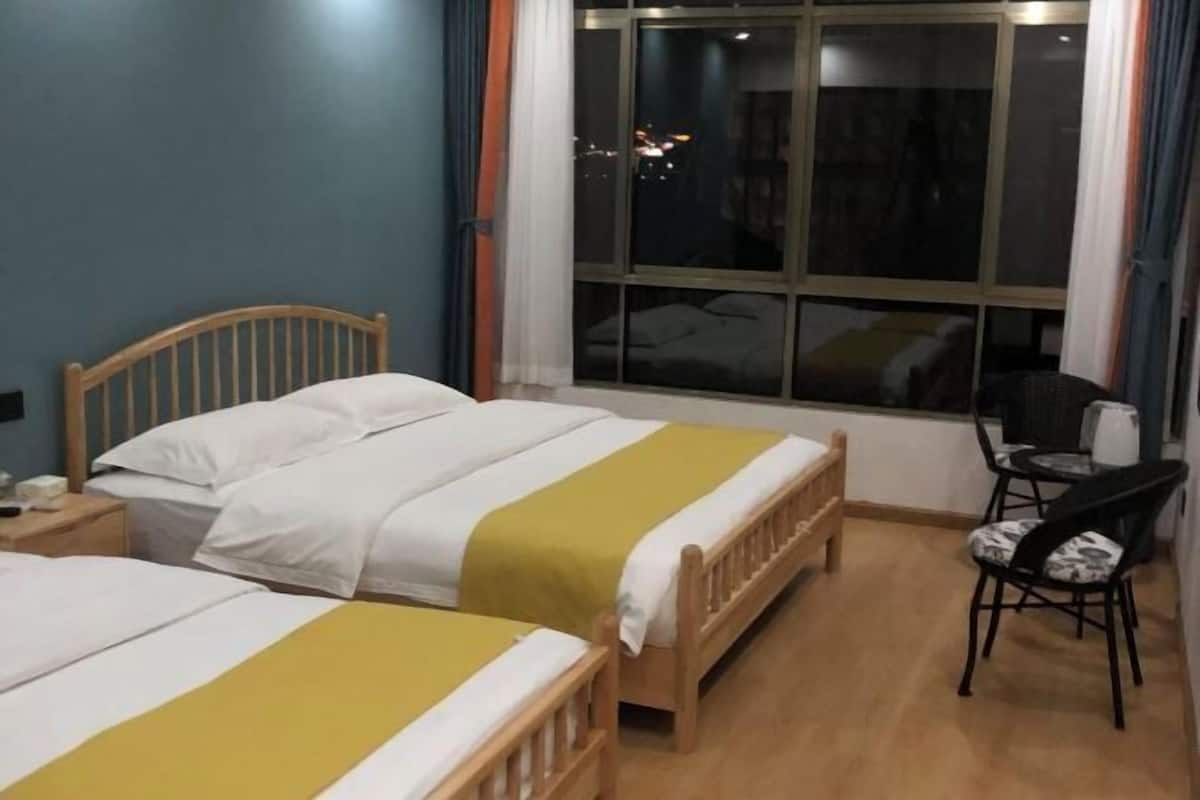 Une chambre d’hôtel avec deux lits, une tête de lit en bois, une fenêtre avec des rideaux, une petite table et une chaise.