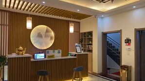 A reception area with a wooden reception desk, two bar stools, a round wall-mounted light fixture, and a staircase in the background. - Lanyu Inn (Yichang Three Gorges Dam) (Yichang)
