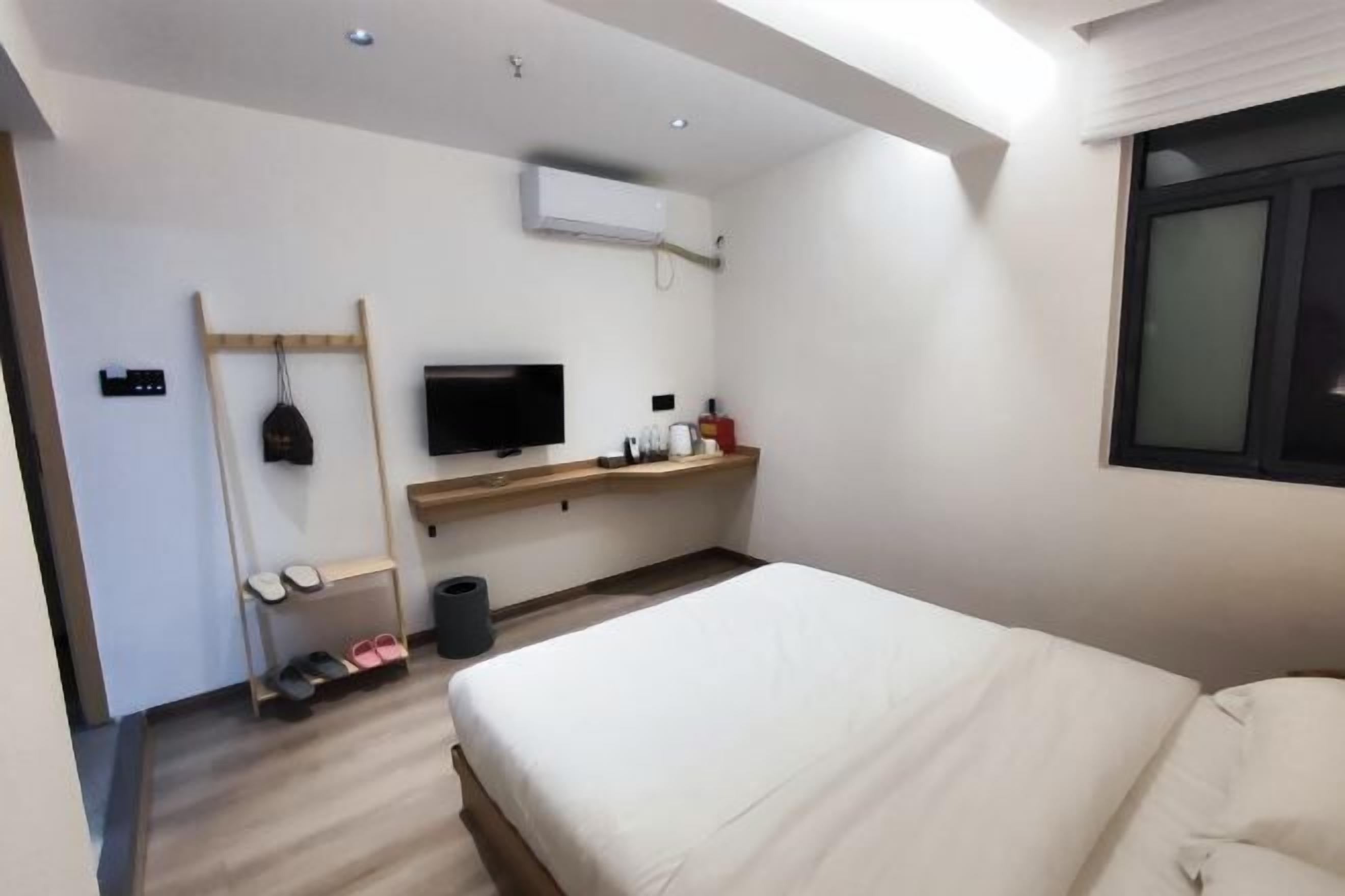 A modern hotel room with a bed, a TV, a shelf with toiletries, and a shoe rack.