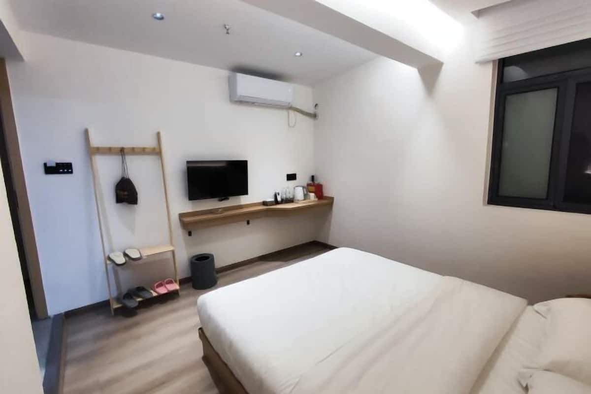Une chambre d’hôtel moderne équipée d’un lit, d’une télévision, d’une étagère avec des articles de toilette et d’un porte-chaussures.