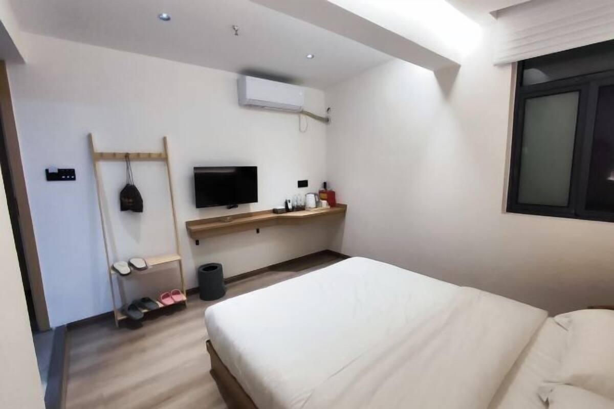 A modern hotel room with a bed, a TV, a shelf with toiletries, and a shoe rack.