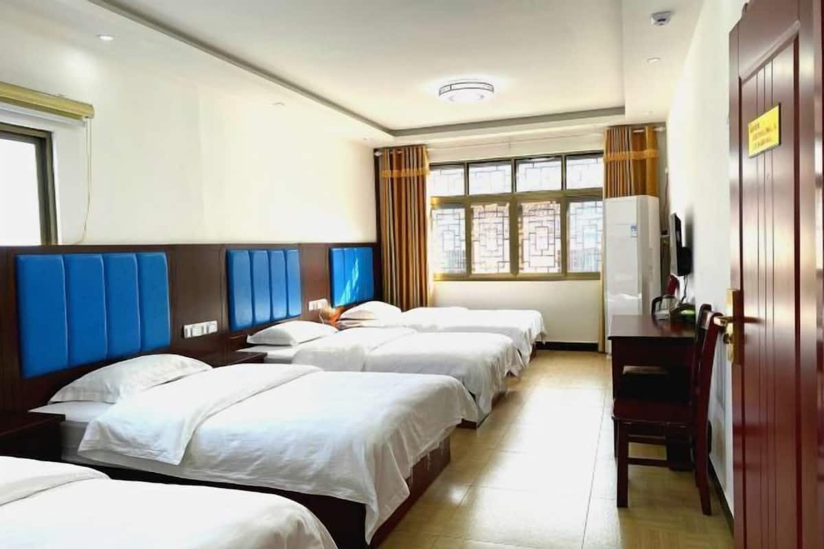 Une chambre d’hôtel avec trois lits, un bureau, une chaise, une télévision et une fenêtre avec des rideaux.