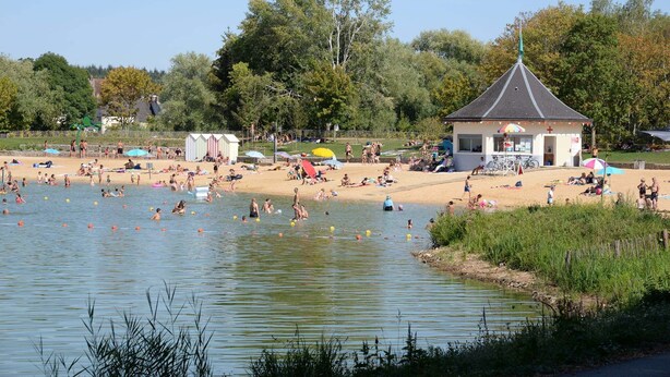 Eine Seenlandschaft mit einem kleinen Pavillon, einem Sandstrand und Menschen bei verschiedenen Aktivitäten.
