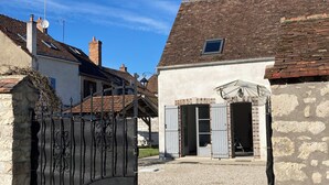 Ein ländliches Anwesen mit einem Schotterweg, der zu einem verschlossenen Eingang führt, ein Steinhaus mit Ziegeldach und ein kleines, angrenzendes Gebäude mit einem Fenster.