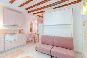 A modern kitchen with pink cabinets, a pink sofa, and a dining area with pink chairs.