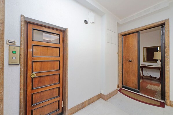 A hallway with a wooden door, a light switch, and a mirror on the wall.