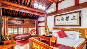 A traditional room with a wooden bed, a red chair, a table with a vase, and a framed sign on the wall. - Yongyichang Inn (Pingyao County)