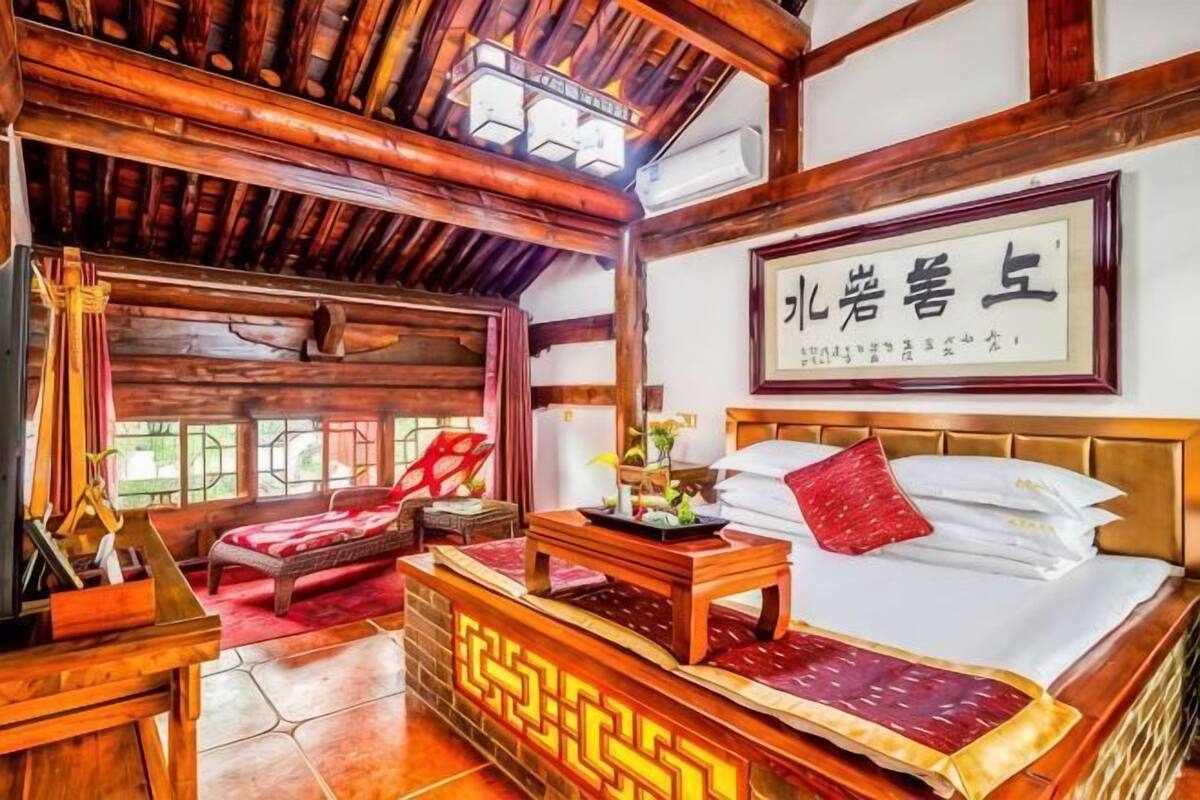 Quarto tradicional com cama, escrivaninha e cadeira. Há um quadro na parede e uma janela com vista.