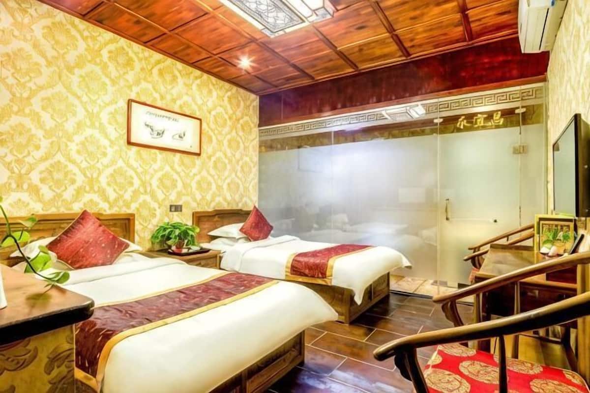Quarto de hotel com duas camas, teto de madeira, parede com desenho estampado e uma pequena mesa com uma planta.
