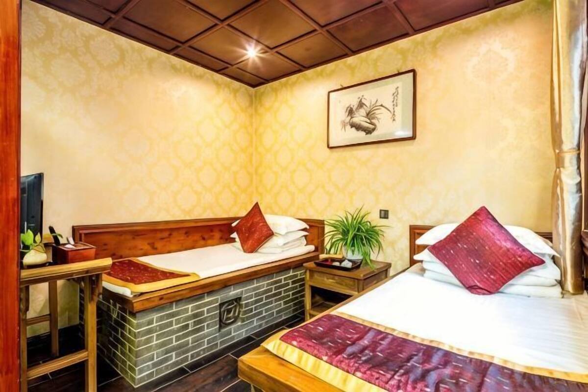Quarto com duas camas, uma escrivaninha de madeira, uma mesinha e um vaso com planta.