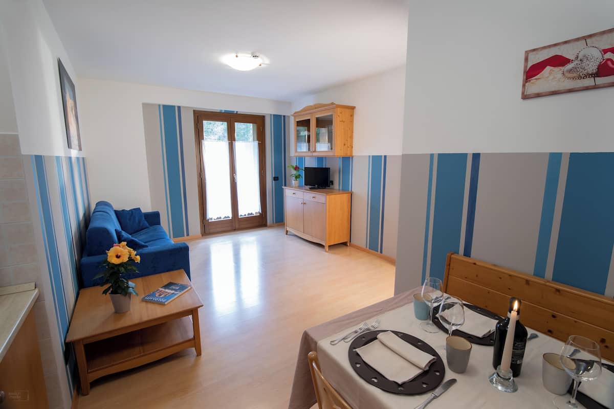 A modern living room with a sofa, a dining table set for two, and a kitchen area with a television.